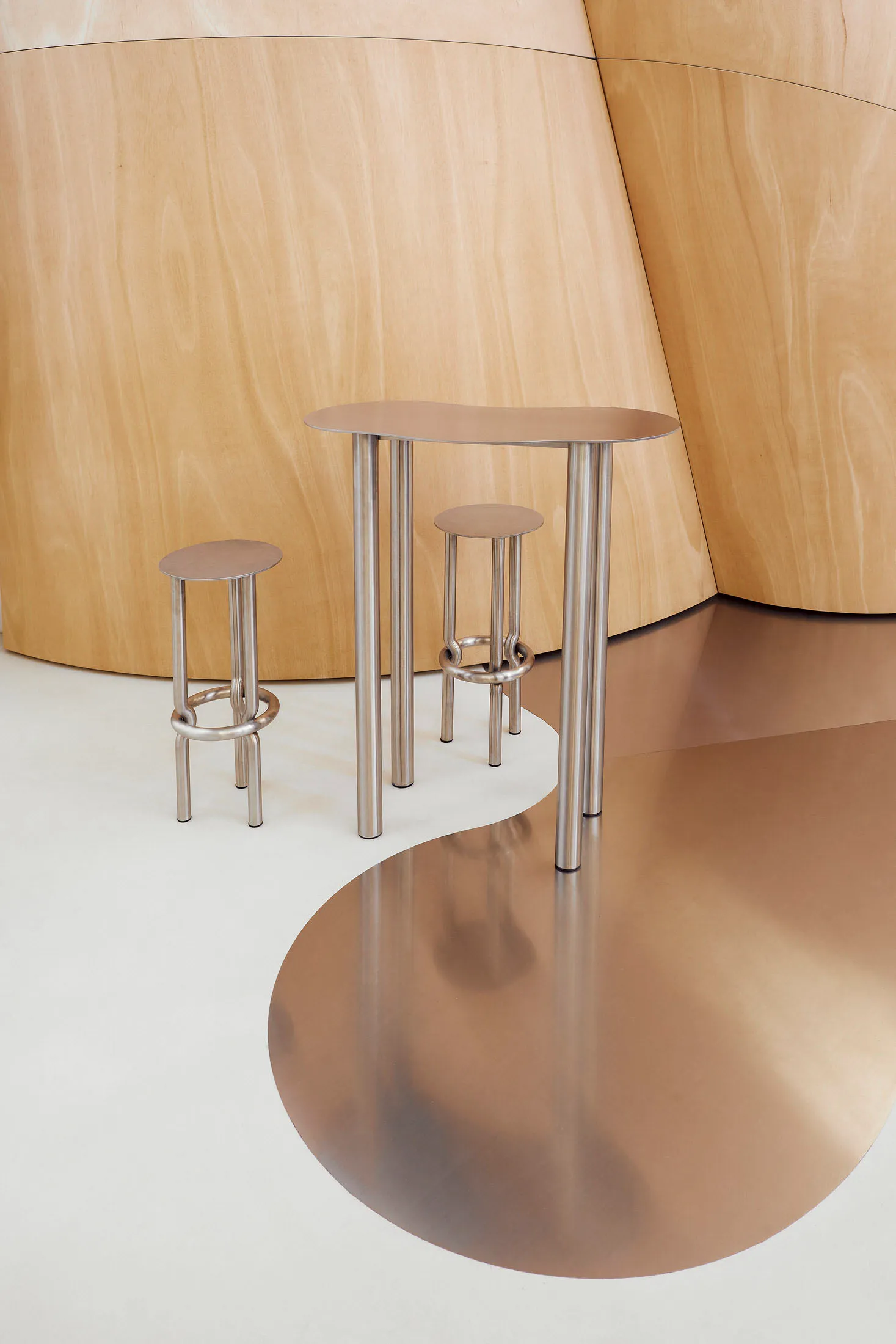 Three modern metal tables with unique curved shapes and stools in a contemporary setting.