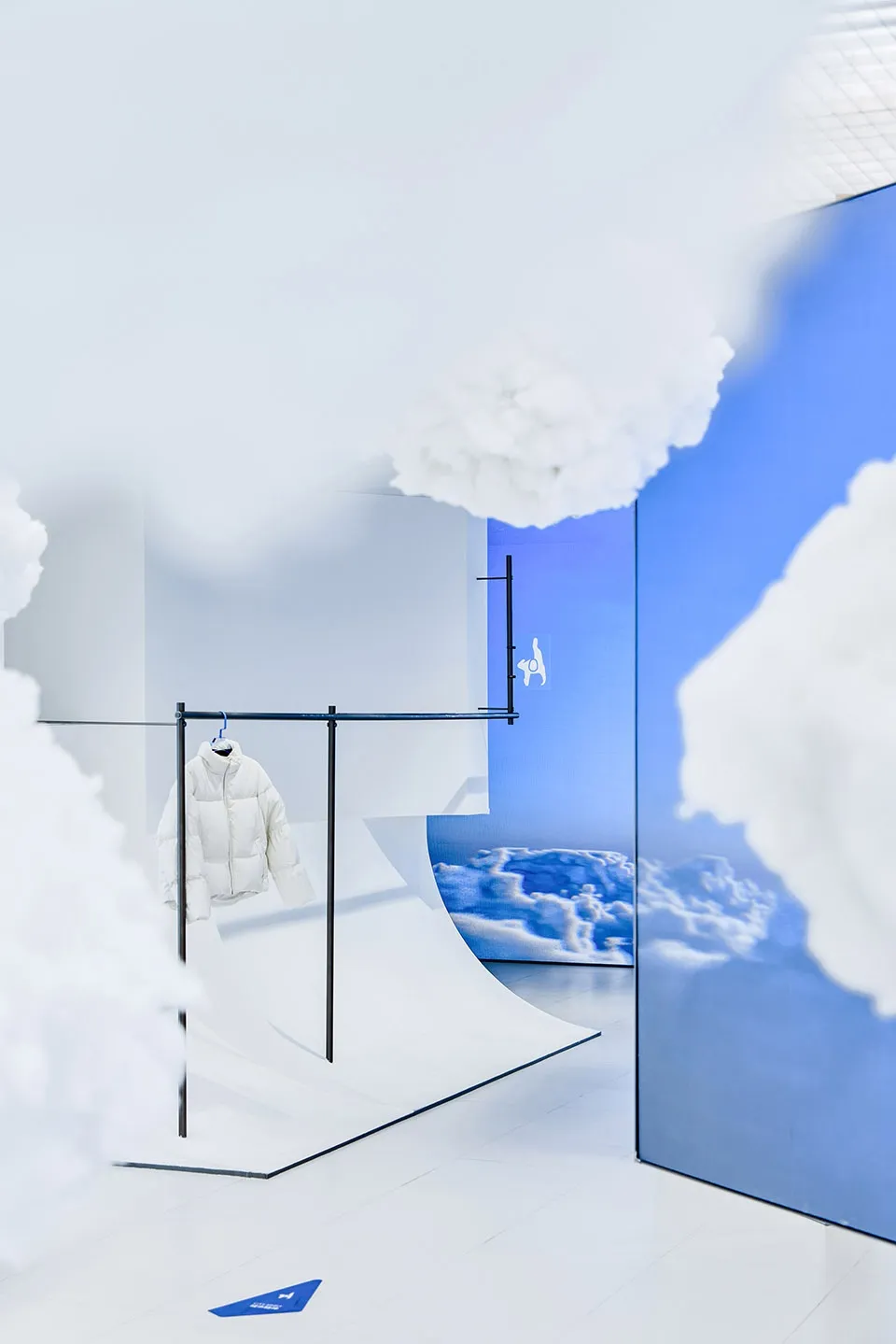 A white jacket hanging on a clothes rack in a shop with cloud-themed decor.
