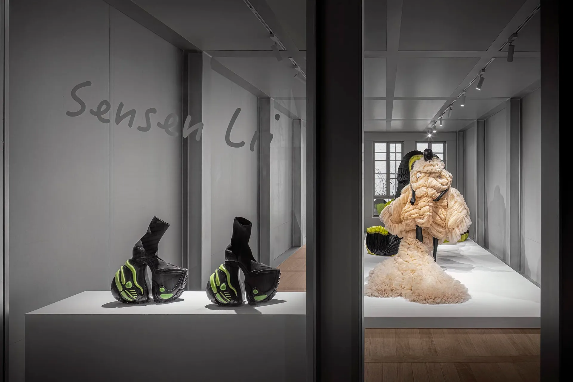 A display featuring futuristic black and green high-heeled shoes and a intricately draped, beige textile piece in an industri