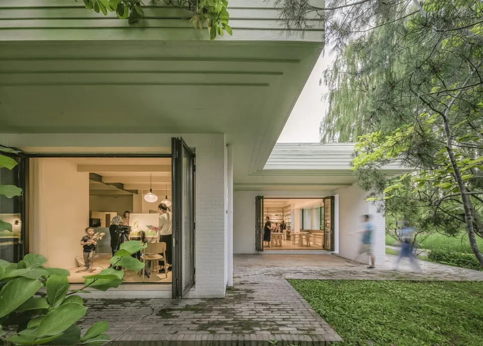 A modern living area with brick walls surrounded by greenery and open folding doors.