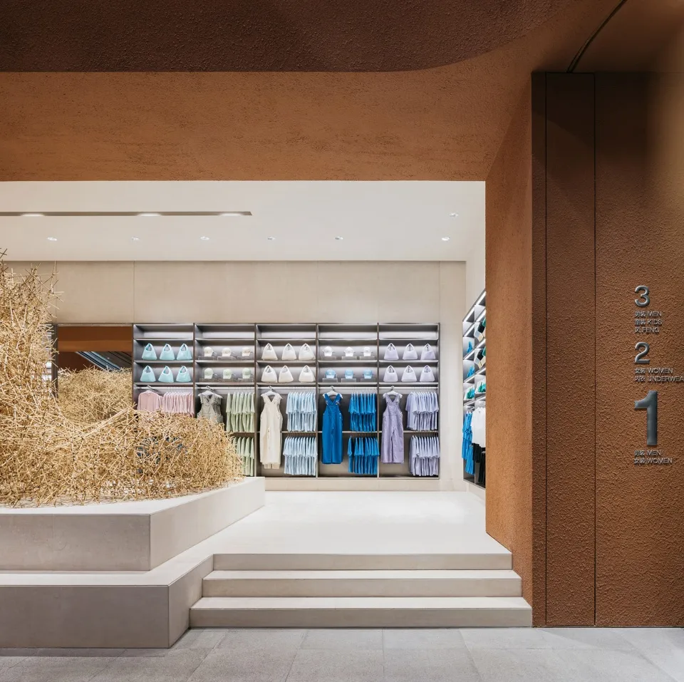 A modern retail storefront with concrete walls and white, pastel, and blue clothing on display.