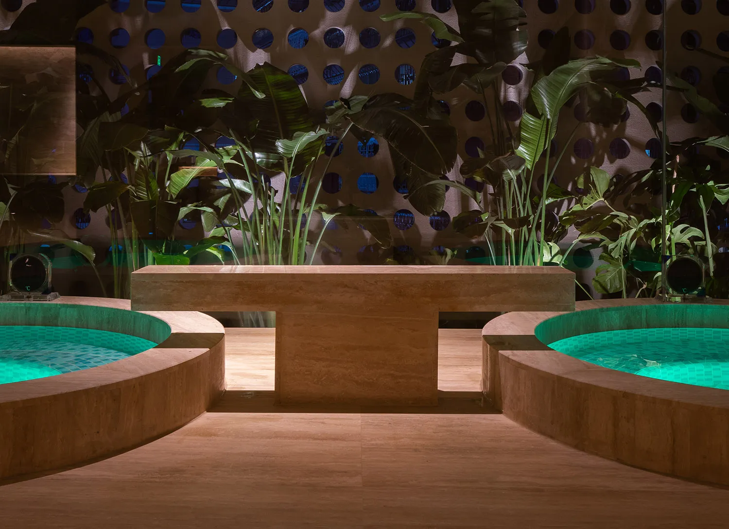 A modern concrete bench placed by a tranquil poolside with lush green plants and a perforated wall backdrop.