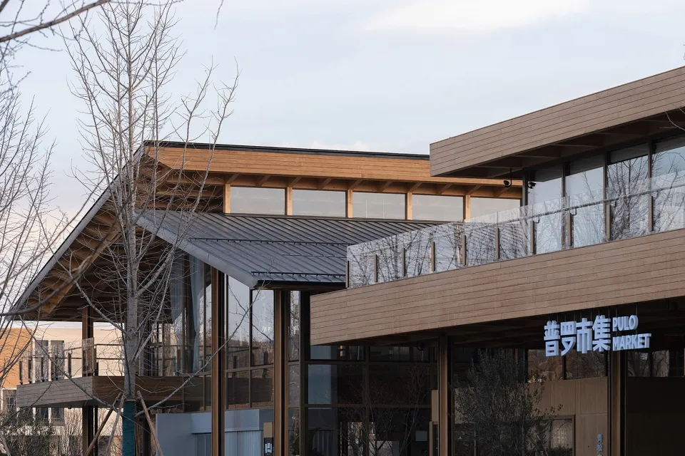 A modern building with a wooden exterior and a metal roof, featuring large glass windows.