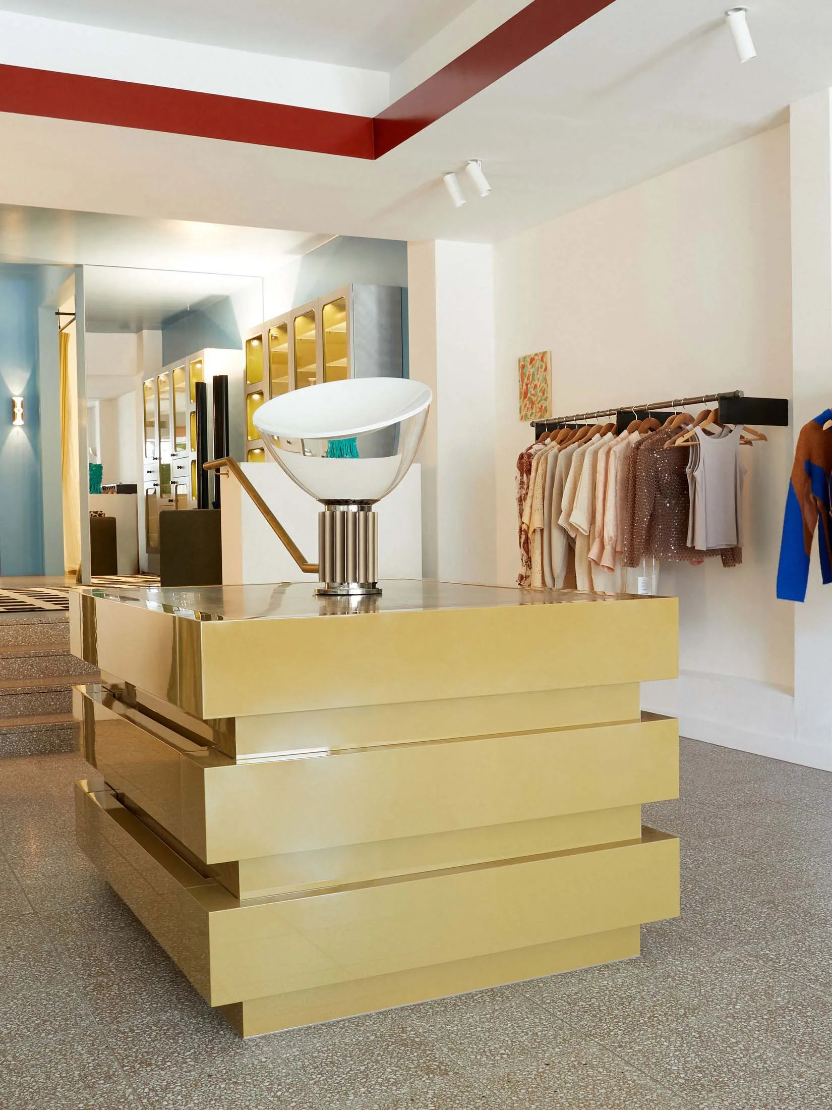 Modern clothing store with brass furniture, featuring a gold pedestal display and clothing racks.