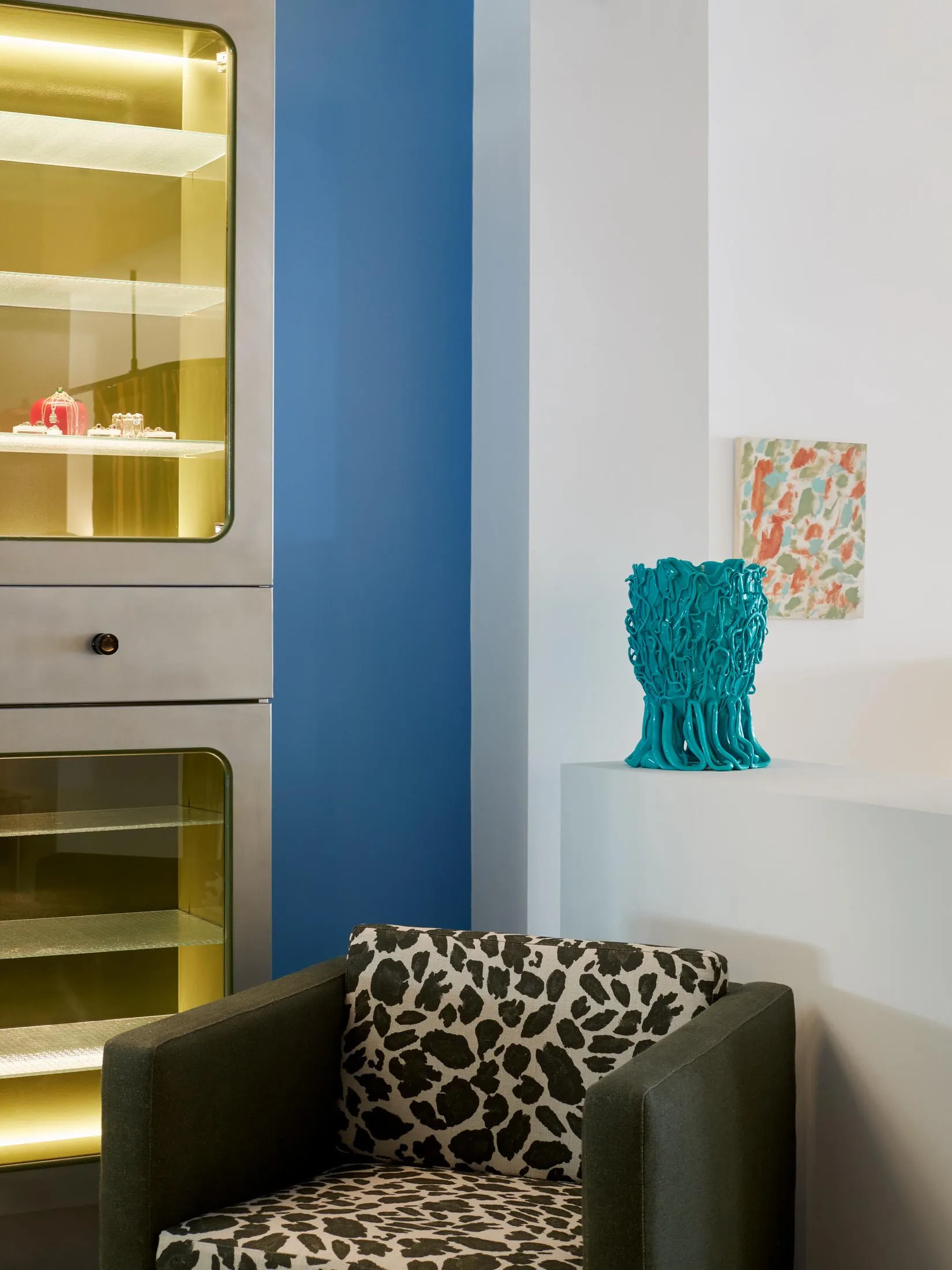 A modern interior living room with a leopard print armchair, a turquoise vase, and a glass-front display cabinet.