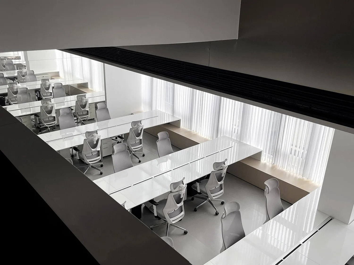 Modern minimalist office space featuring white surfaces and desks with gray office chairs.