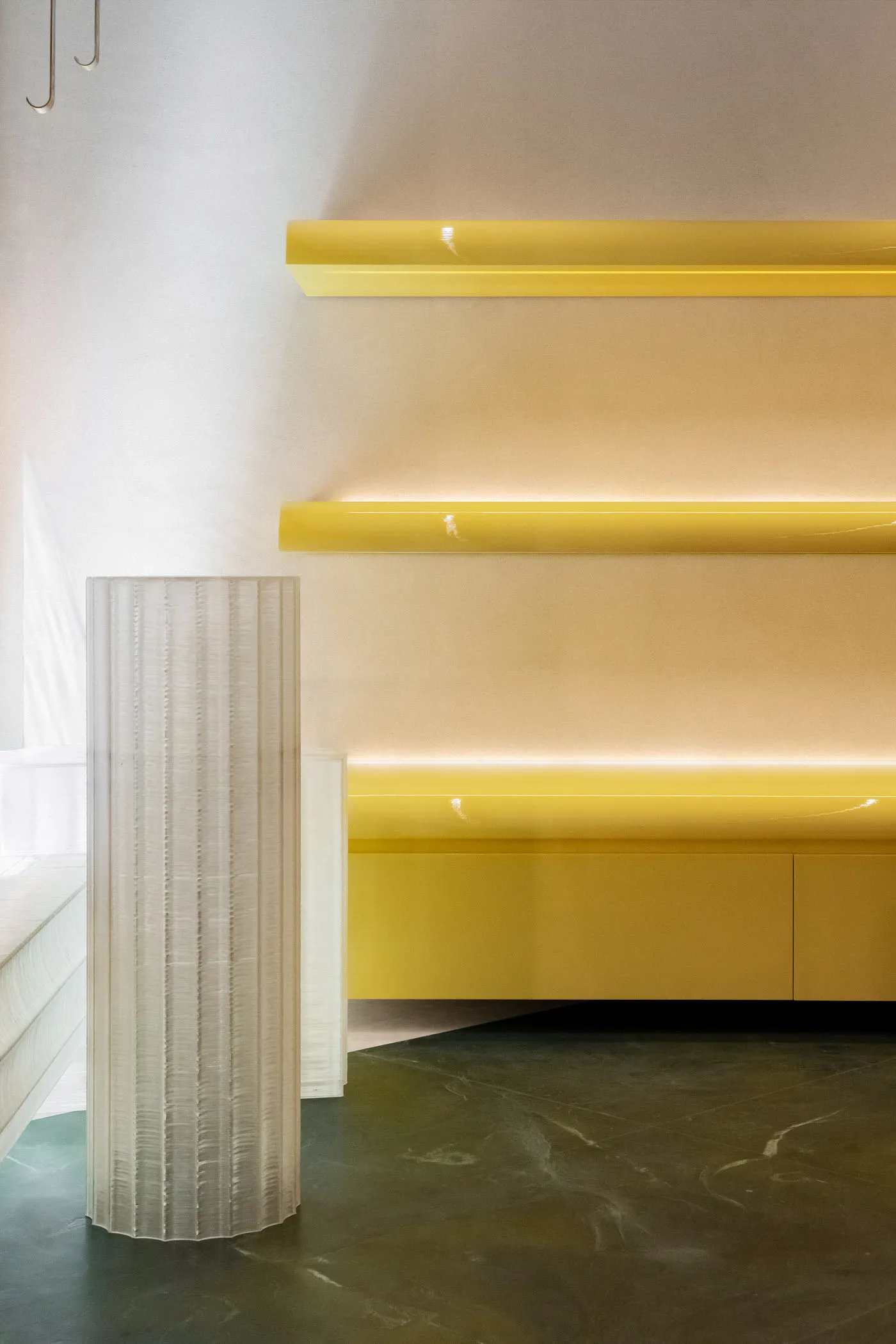A minimalist retail storefront featuring yellow columns, white shelves, and a white floor.