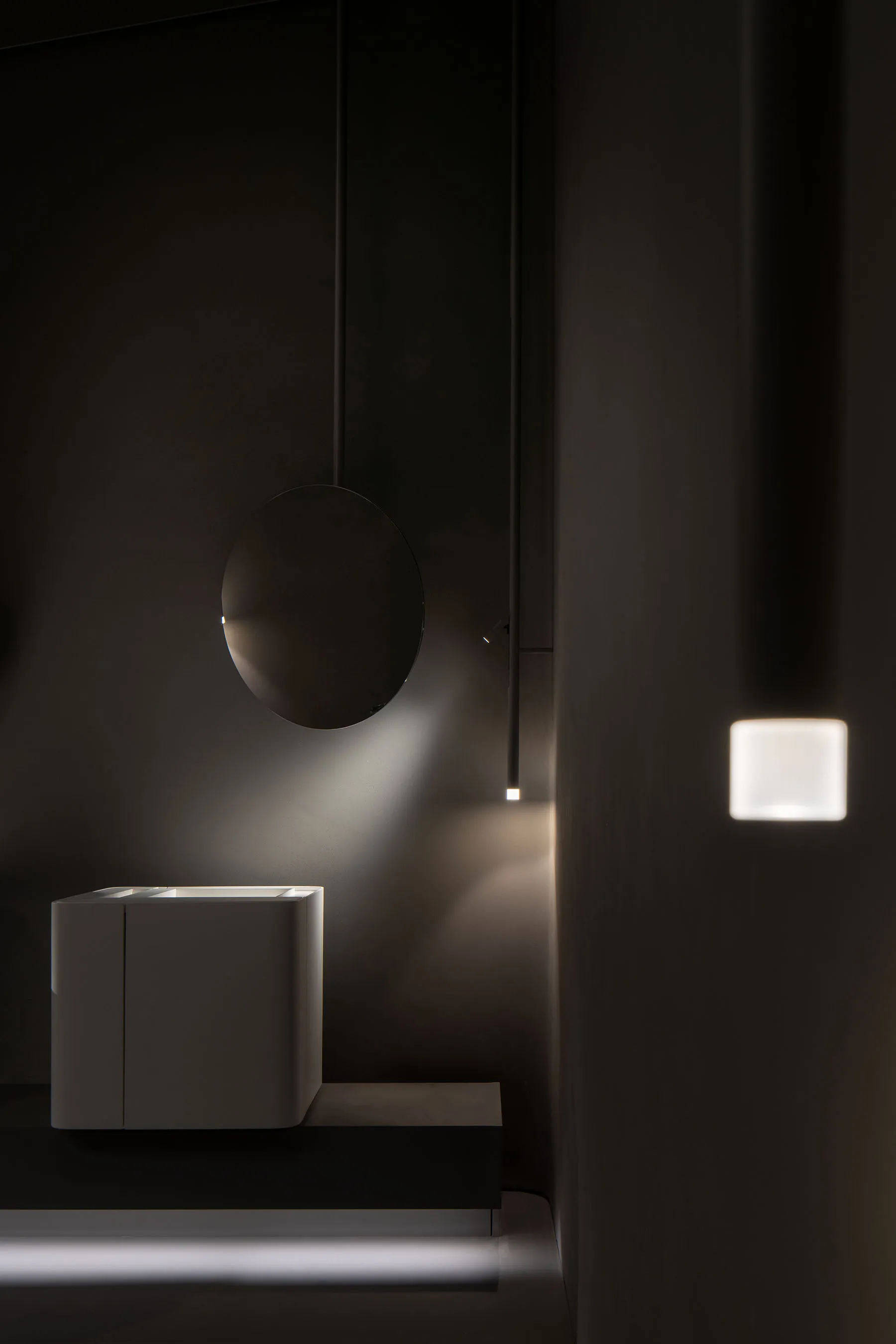 Modern minimalist bathroom with white ceramic sink, round mirror, and wall-mounted light fixture.