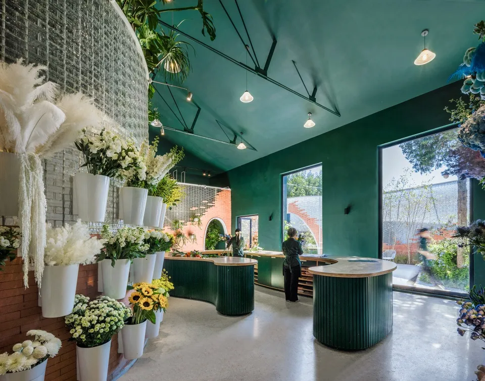 A modern coffee shop interior with green painted walls, brick accents, decorative flowers, and white feather arrangements.