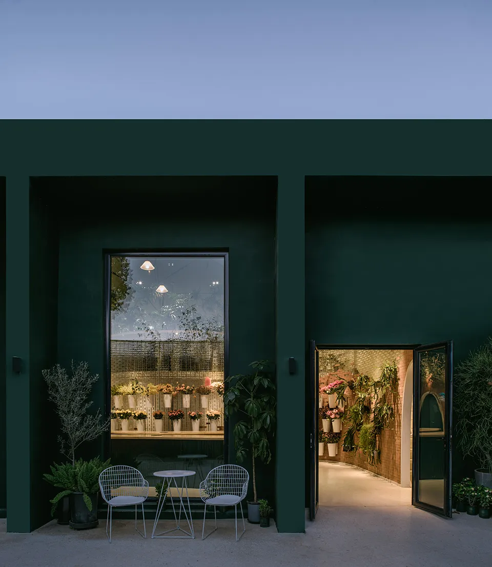 A modern flower shop exterior with green painted walls and large windows displaying various plants.