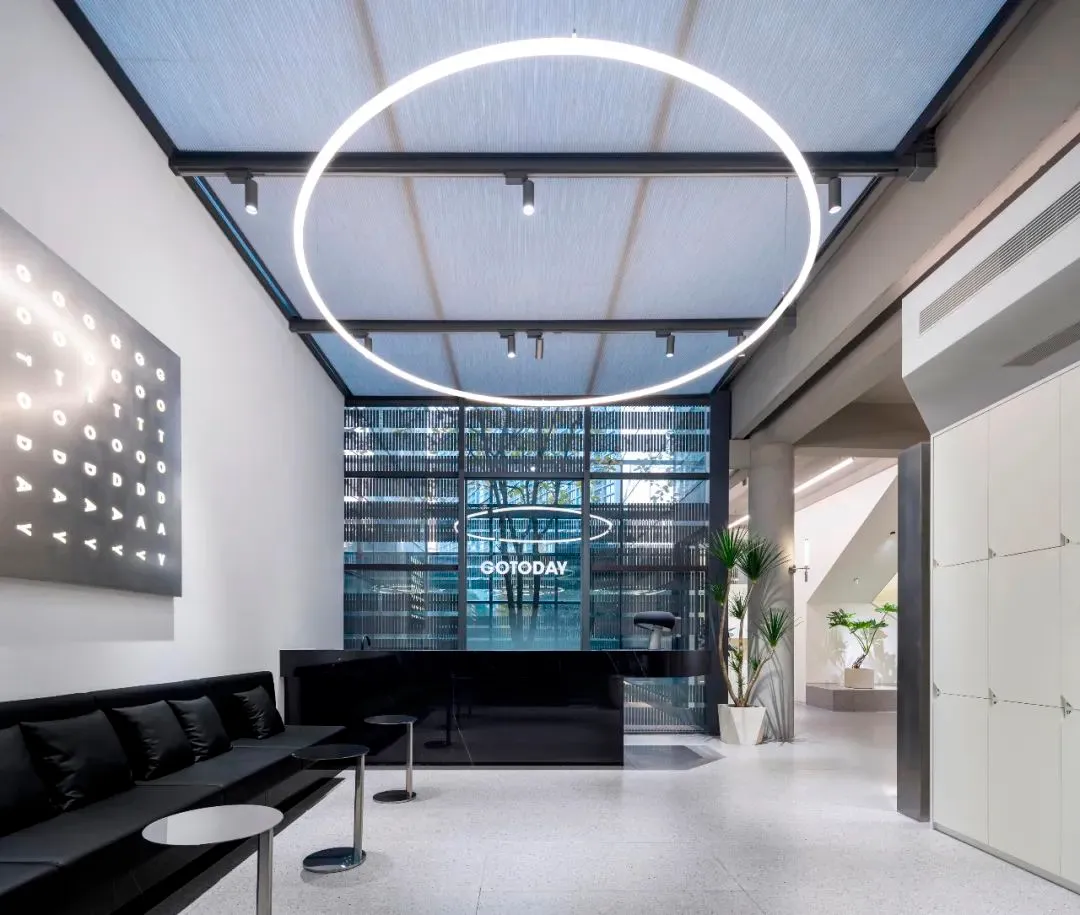 A modern industrial office lobby with a circular light fixture, black furniture, and concrete flooring.