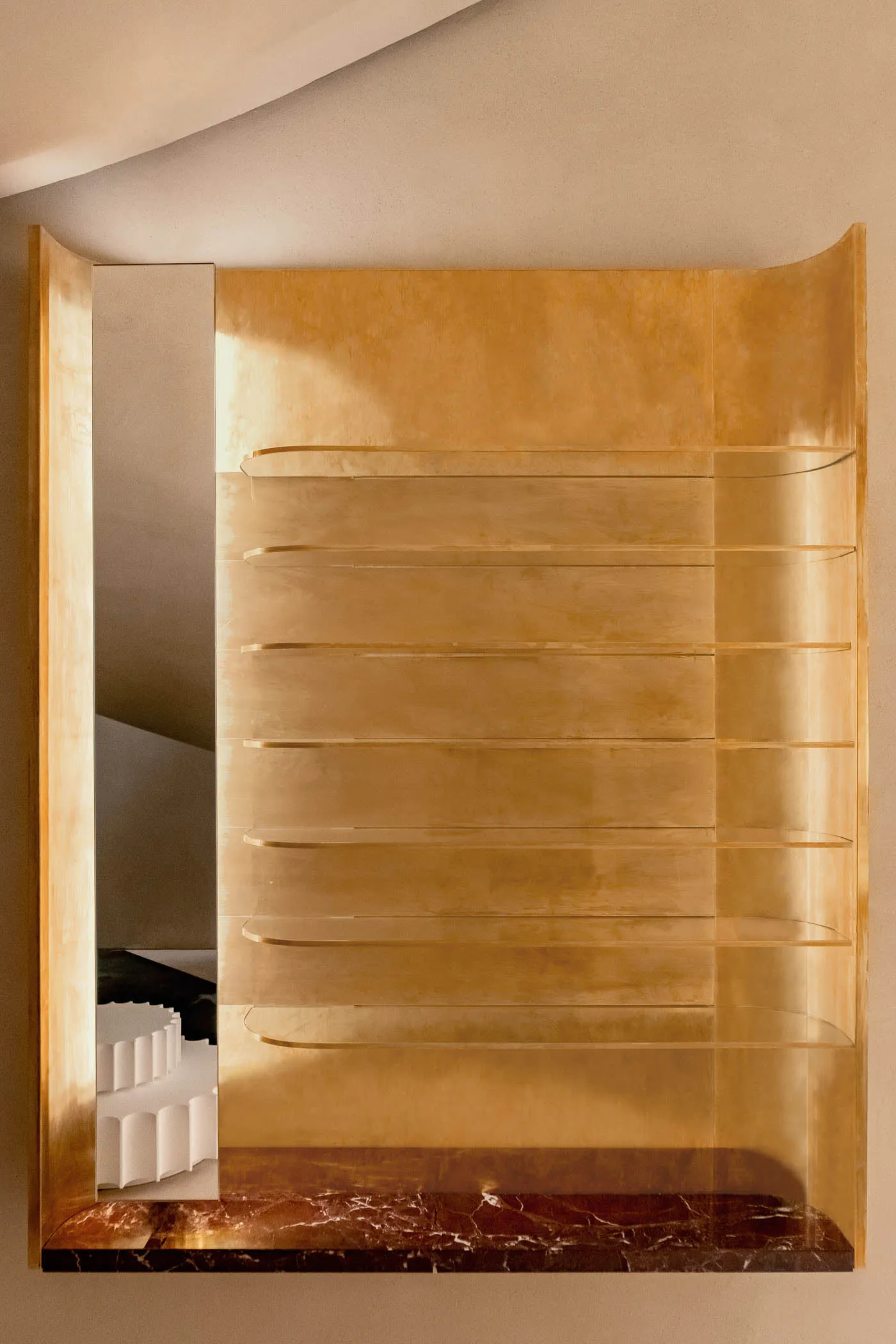 A modern, metallic shelf unit with glass shelves mounted on a white wall, providing a sleek and contemporary design element.