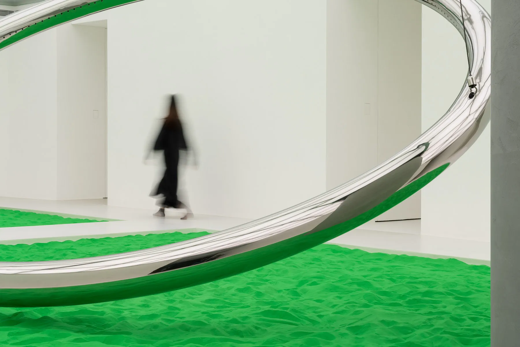 一件現代裝置藝術作品,展現大型曲面金屬結構與綠沙地面。