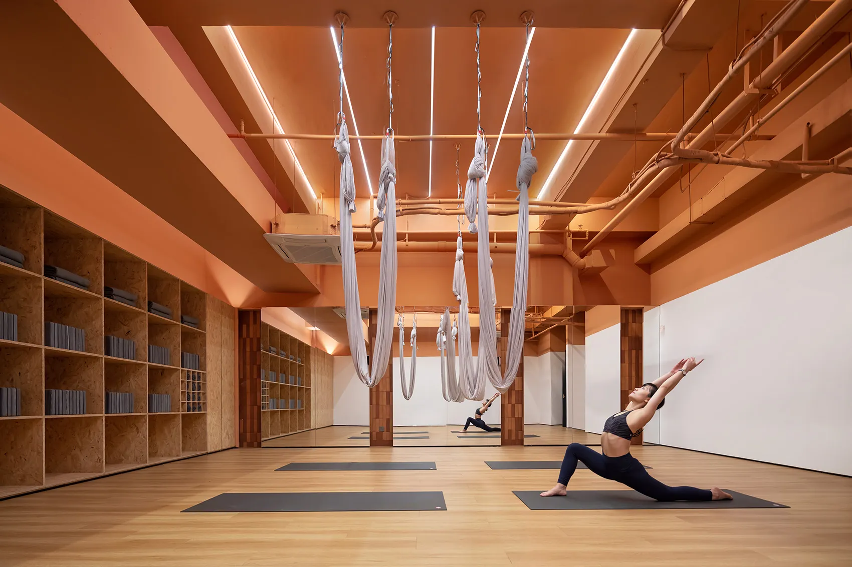 A woman practicing yoga in a minimalist fitness studio with hanging ropes.