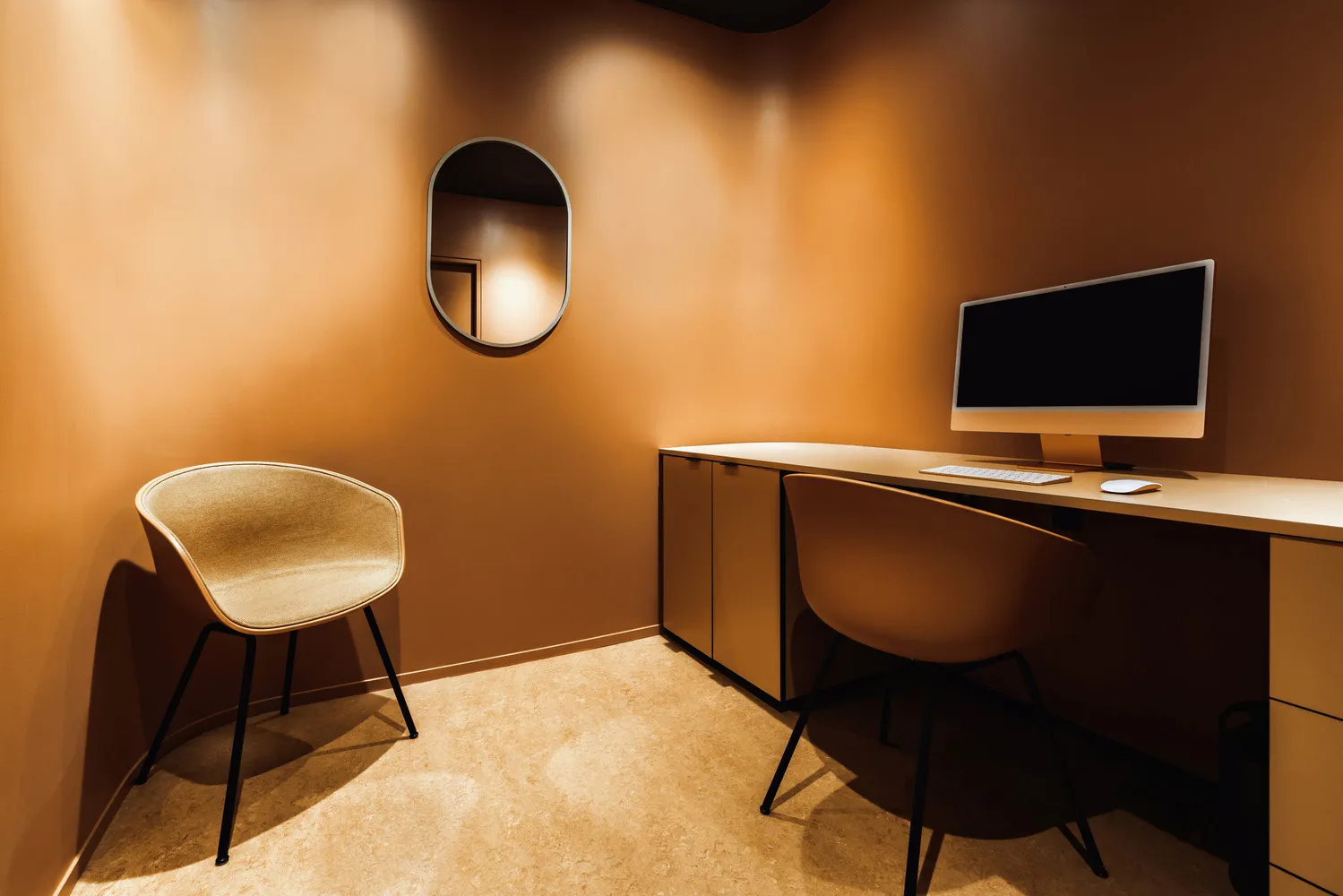 A modern minimalist workspace with a wooden counter, featuring two chairs and a desk with a computer setup.