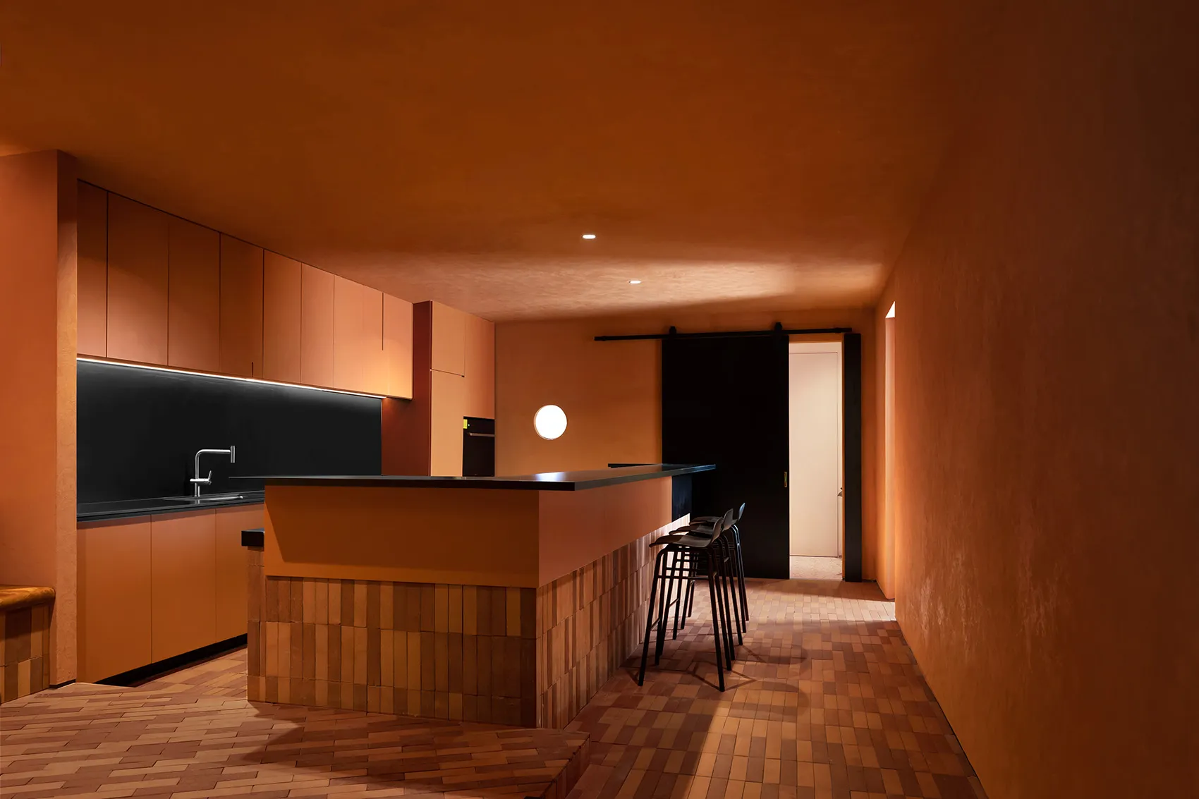 A modern residential kitchen with wooden flooring, cabinets, and stools.