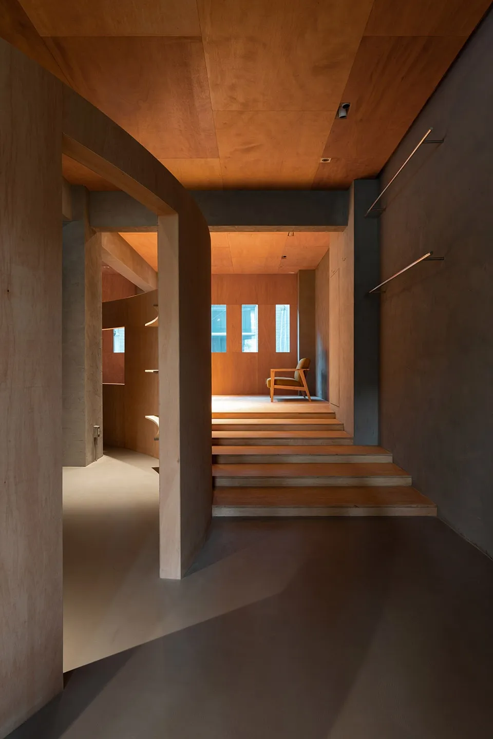 A minimalist wooden interior space with a staircase and a chair.