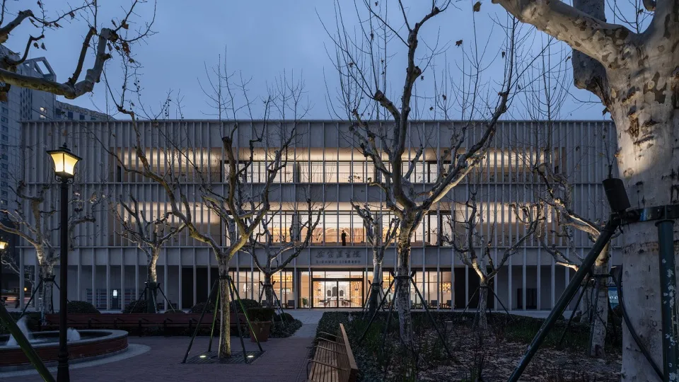 A modern metallic exterior building at dusk with illuminated windows.
