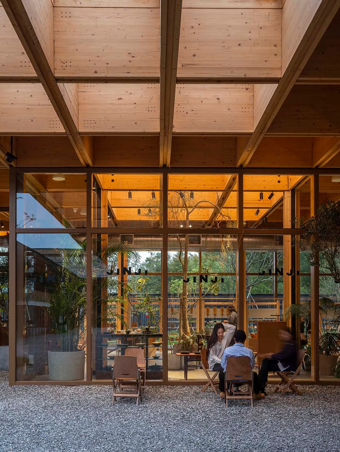 A modern, industrial-style restaurant interior with wooden structural beams and large glass windows.