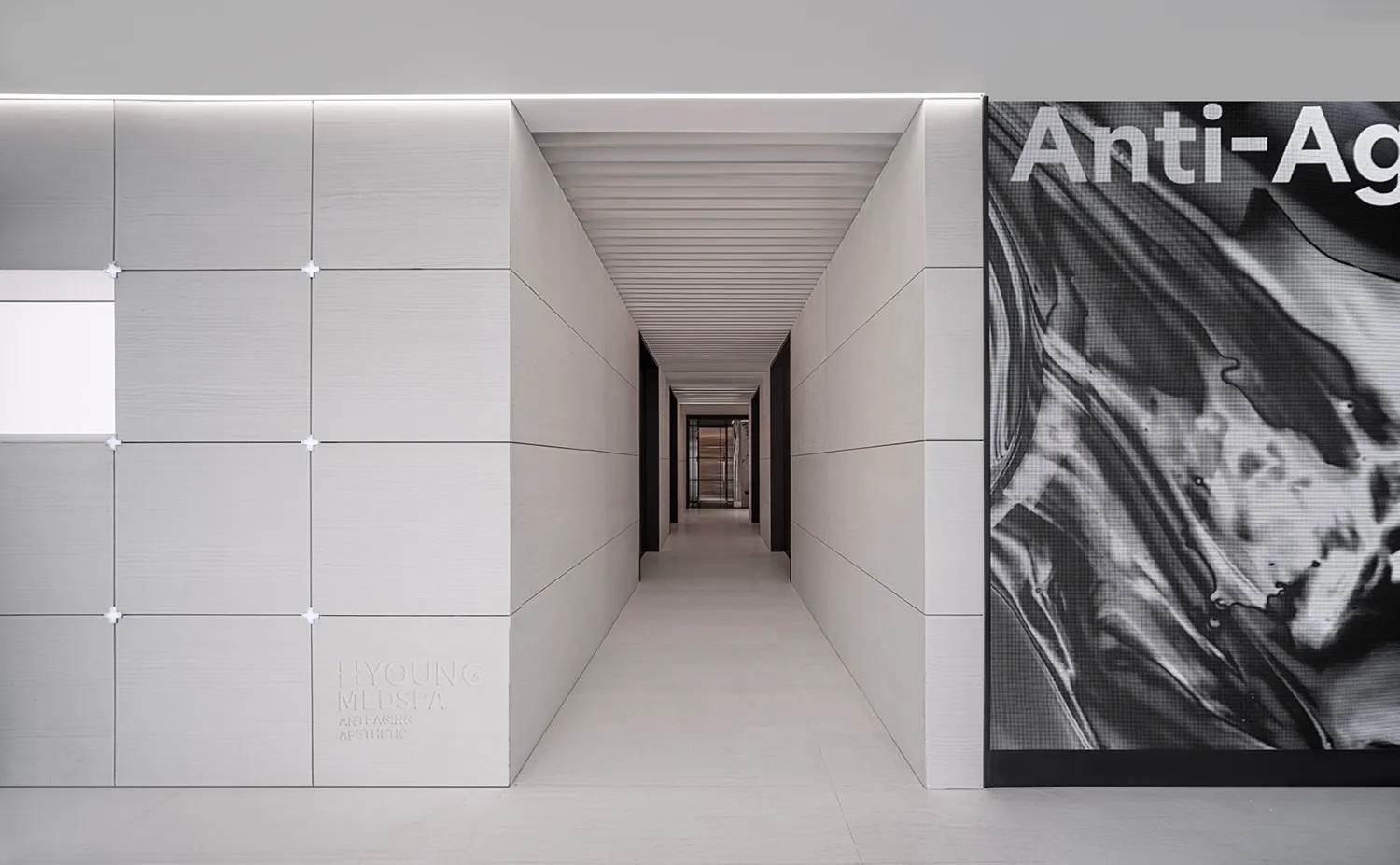 A minimalist corridor with concrete walls and flooring, featuring a large 'Anti-Ageing' artwork.