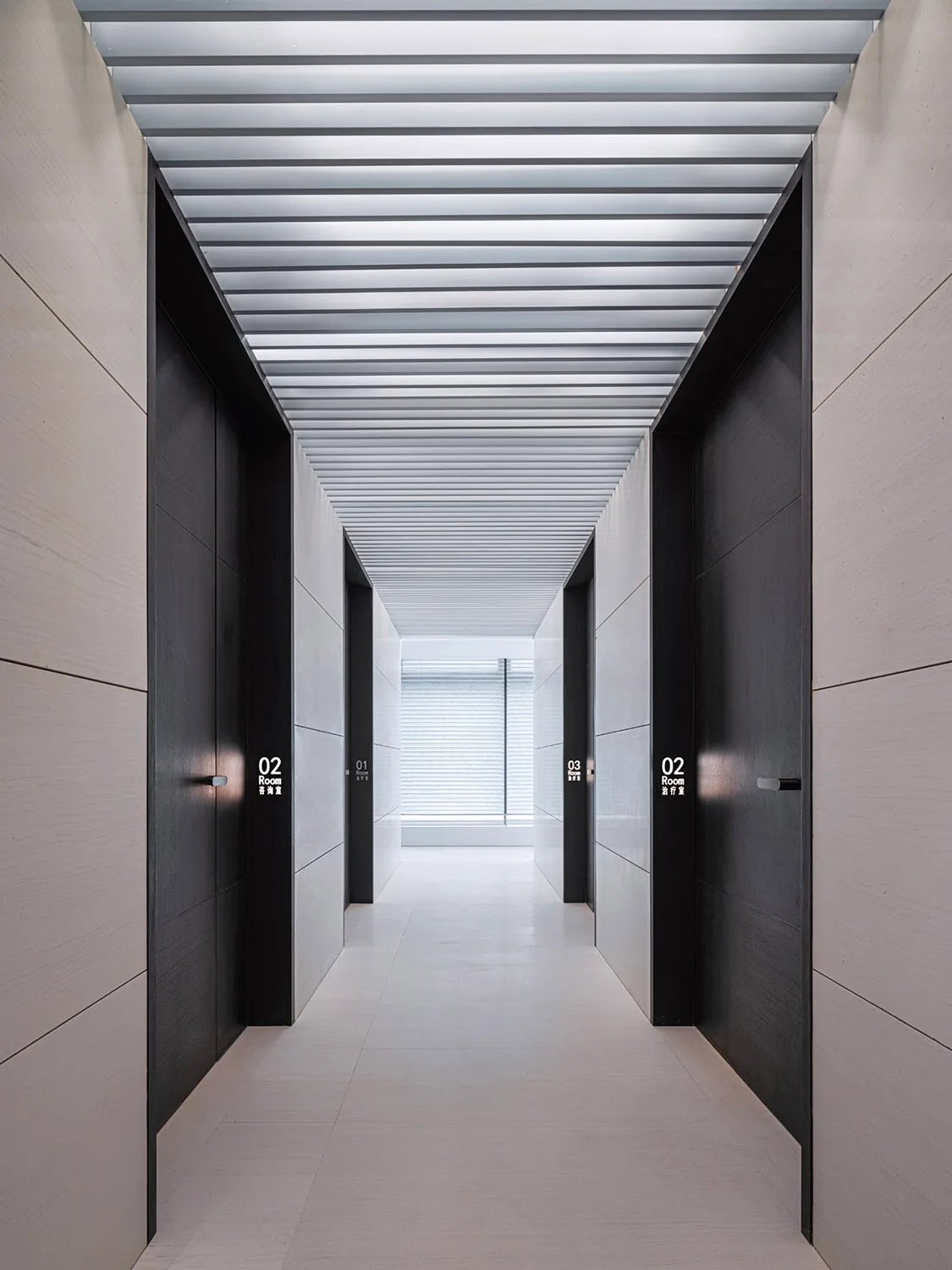 Modern minimalist corridor with white concrete walls and floor, black doors, and a metallic ceiling.