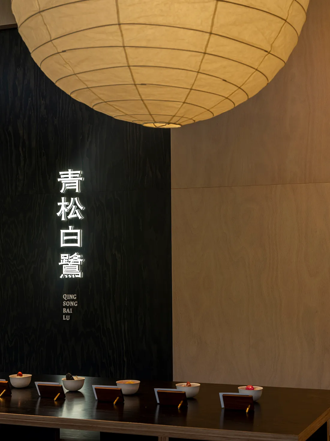 A modern restaurant interior with wooden walls and a large paper lamp hanging overhead.