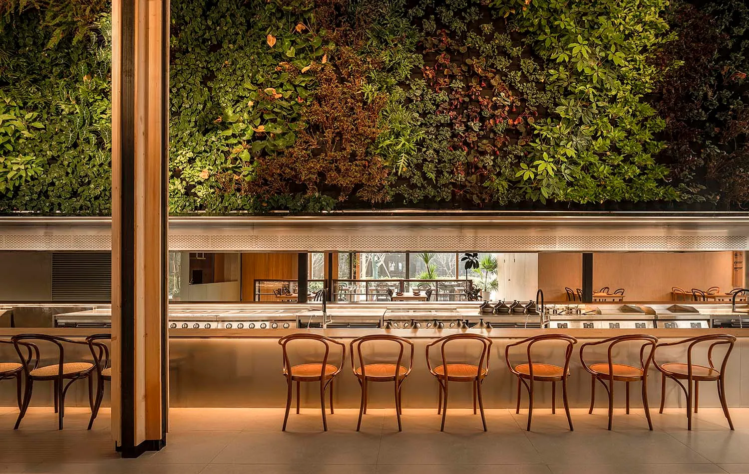 Modern restaurant interior featuring green vertical garden walls, wooden furniture, and a central bar counter.