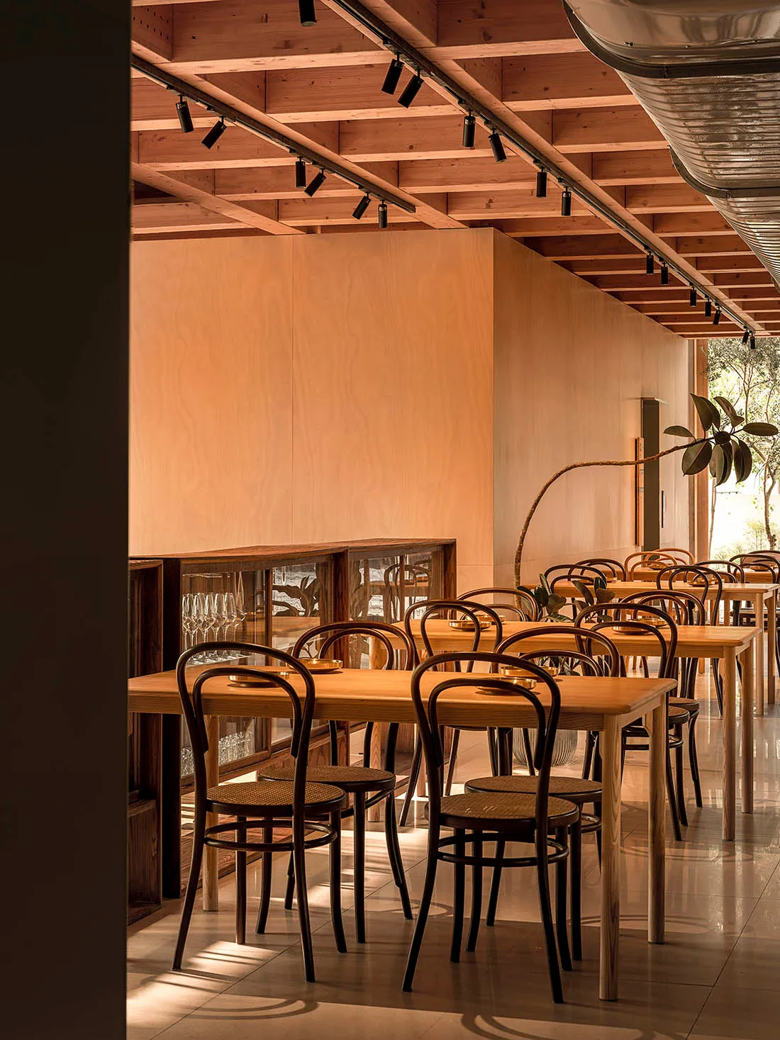 A modern restaurant interior featuring wooden tables and chairs, with exposed wooden beams on the ceiling and a large window