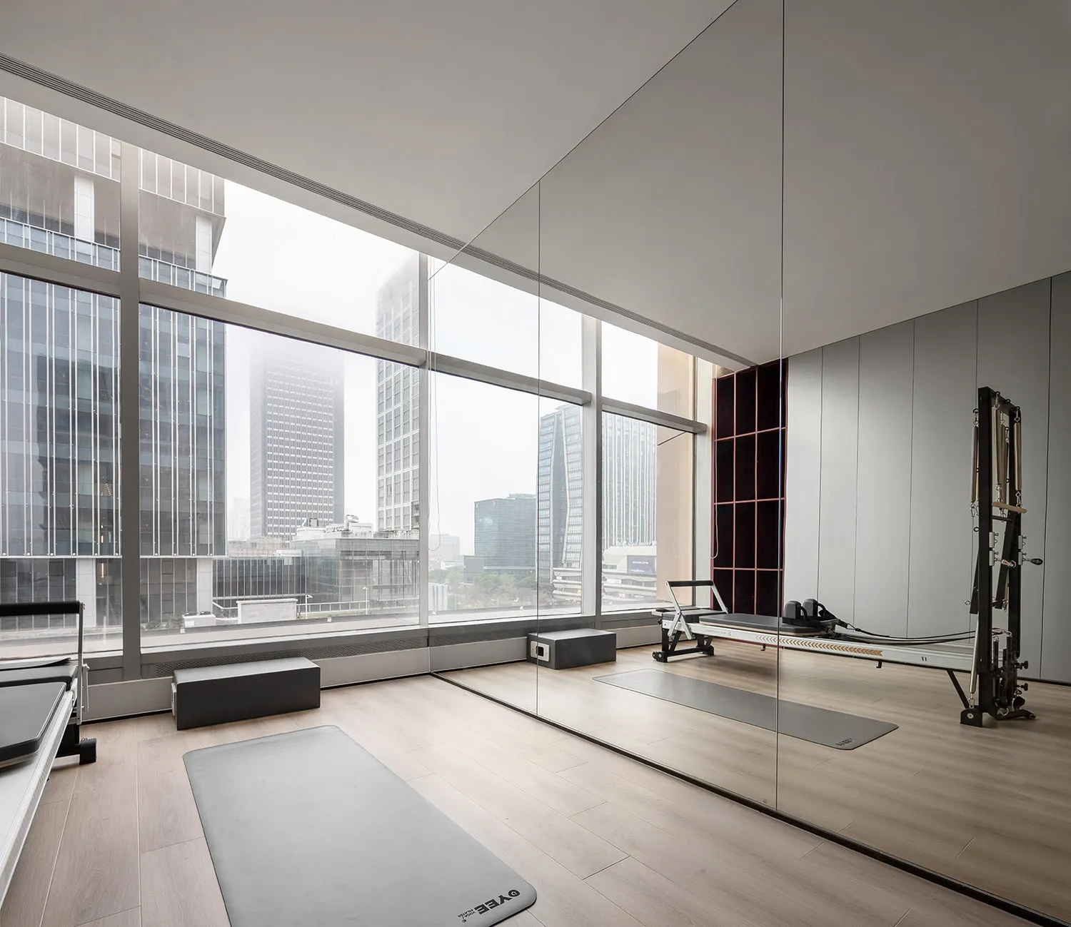A modern workout room with wooden floors and large windows reflecting a cityscape.