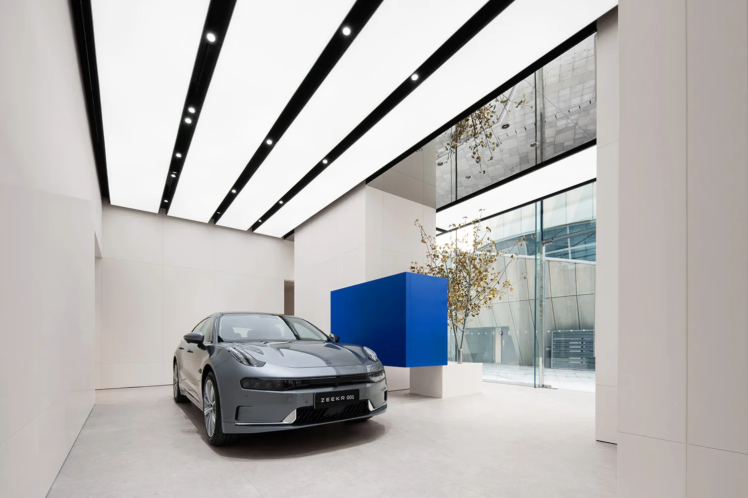 High-angle view of a sleek, modern showroom with a luxury car on display, illuminated by linear lighting and surrounded by mi