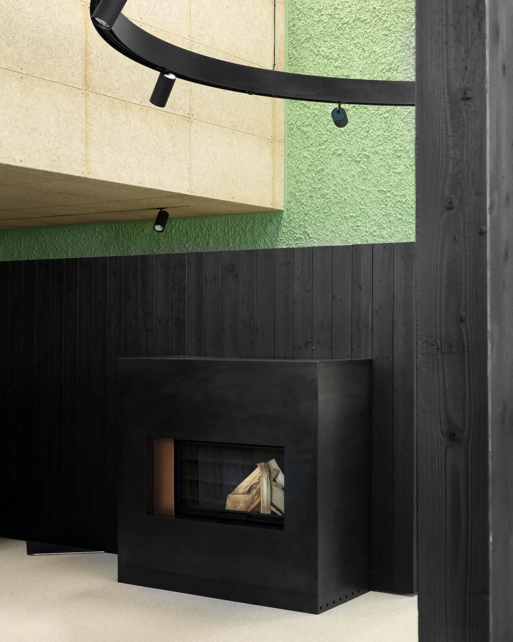 A minimalist black metal fireplace surrounded by black wooden panels and concrete walls.