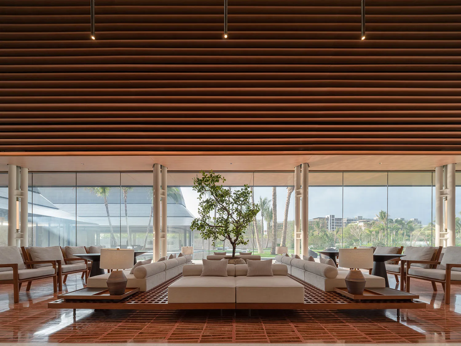 Modern resort lobby featuring wood and concrete materials, with seating arrangements and a central tree.