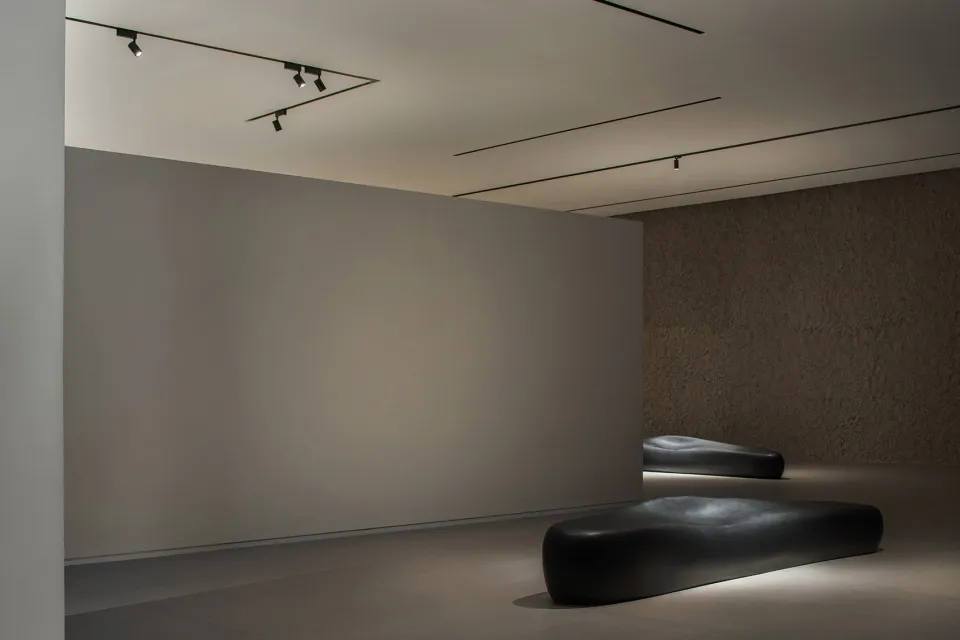 Minimalist modern interior space featuring smooth, textured concrete walls and floors, with contemporary seating and lighting