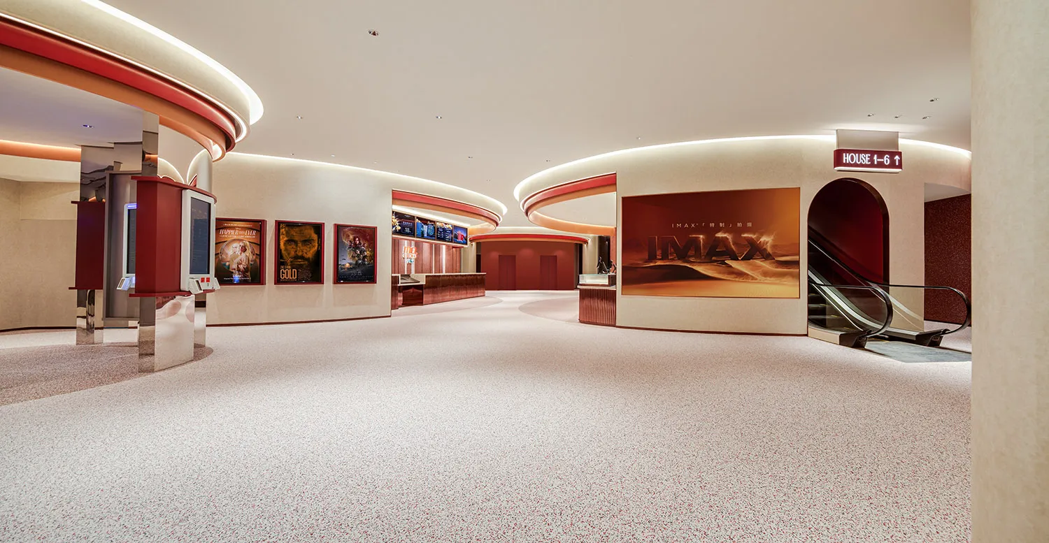 Modern cinema hall interior featuring terrazzo and concrete materials, with movie posters and an escalator.