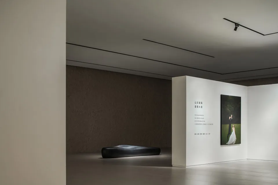 Modern minimalist photography gallery with a minimalist installation featuring a black bench and a framed photograph on the w