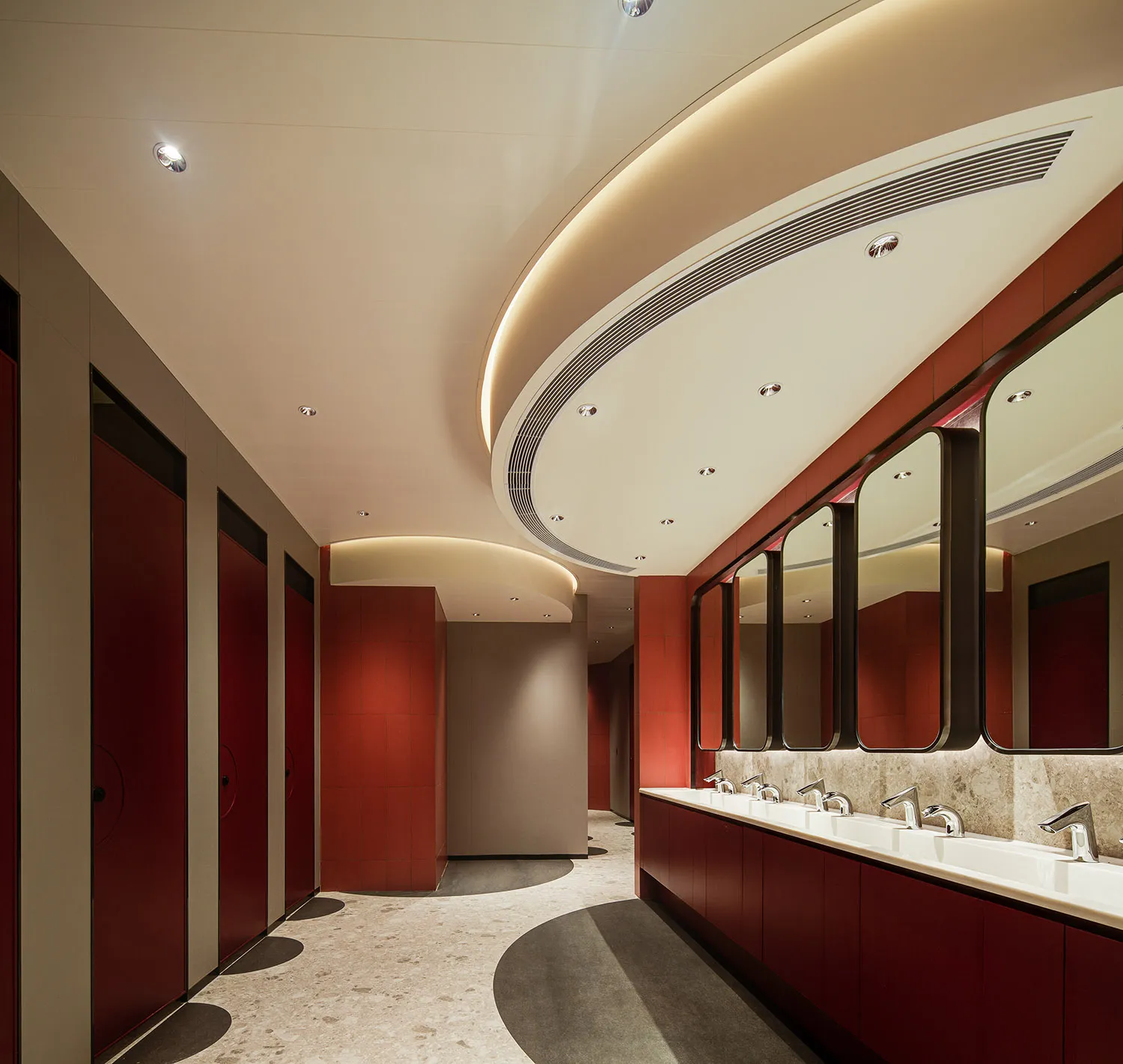 Modern public restroom with red tiles and white walls, featuring sinks, mirrors, and red stalls.