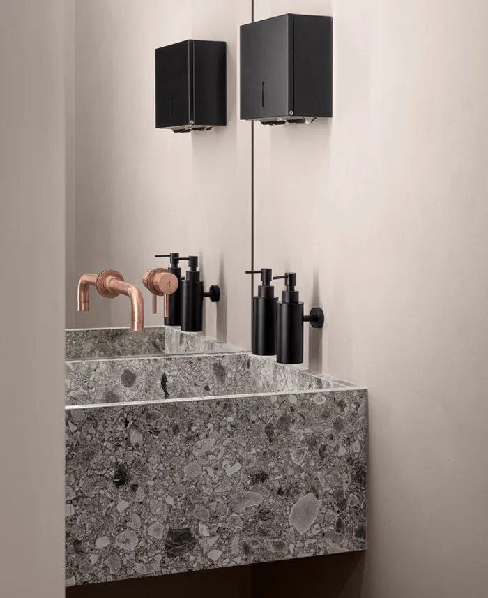 Modern, minimalist bathroom with a sleek concrete countertop and bronze faucets.