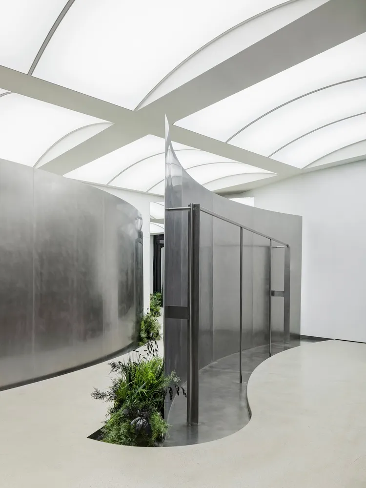 A modern interior design featuring a metallic corridor with green plants and a curved wall.