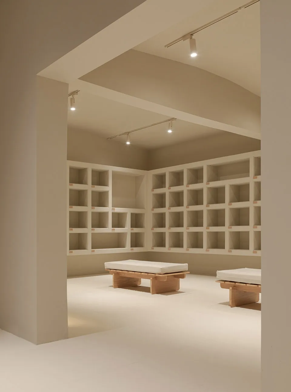 A minimalist storage wardrobe with white wood structure and white cushions on benches in a well-lit room with a neutral color