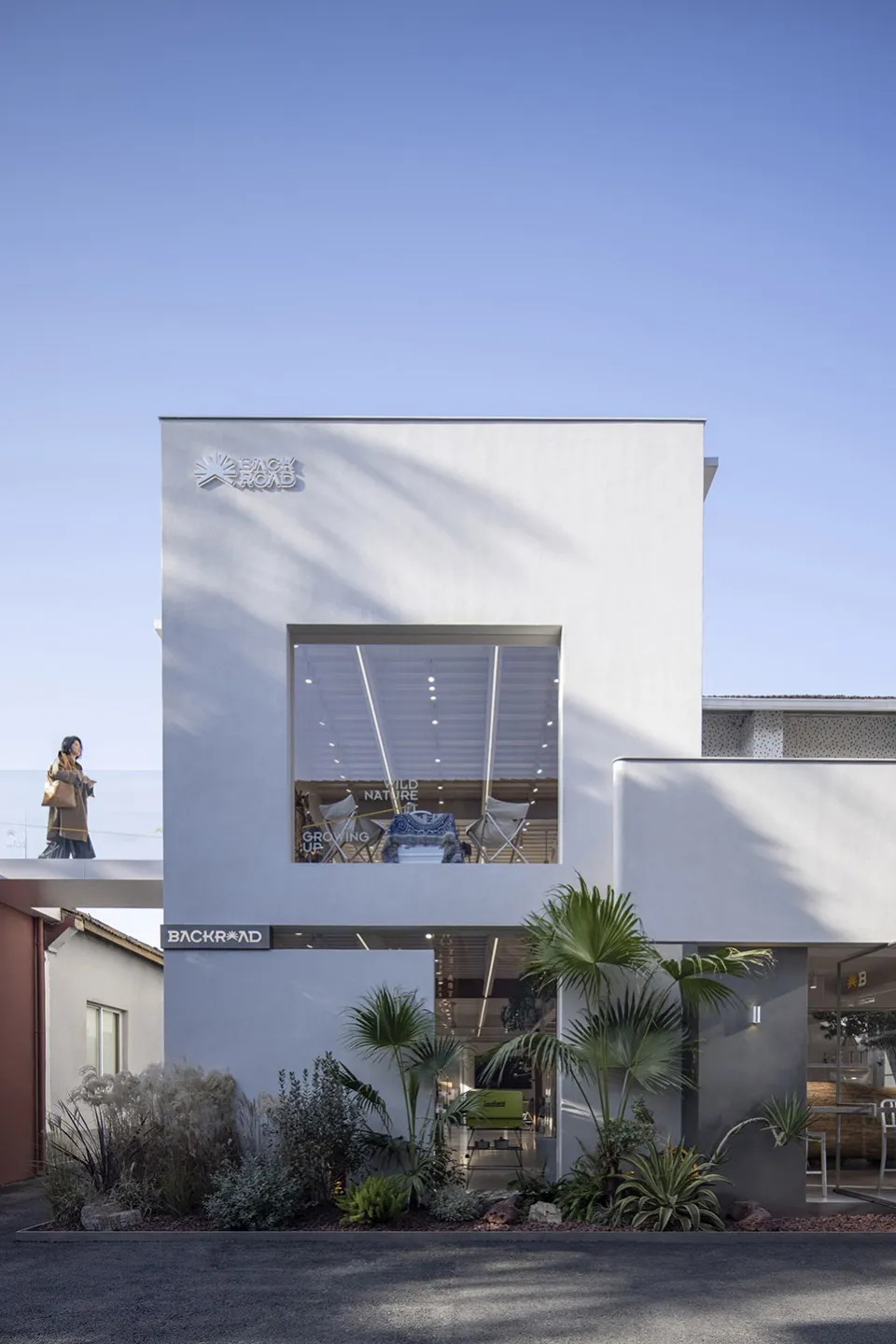 Modern retail storefront with white-rendered and concrete materials, large open window showcasing interior.