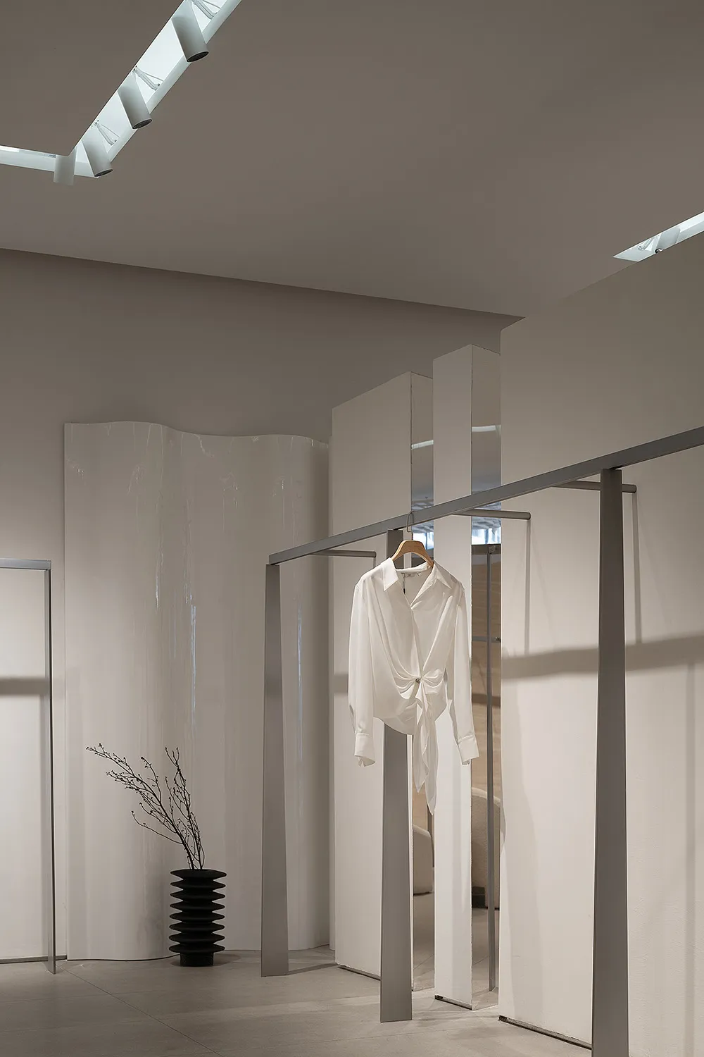 Modern minimalist clothing store interior with white walls, glass panels, and a single white blouse hanging on a rail.