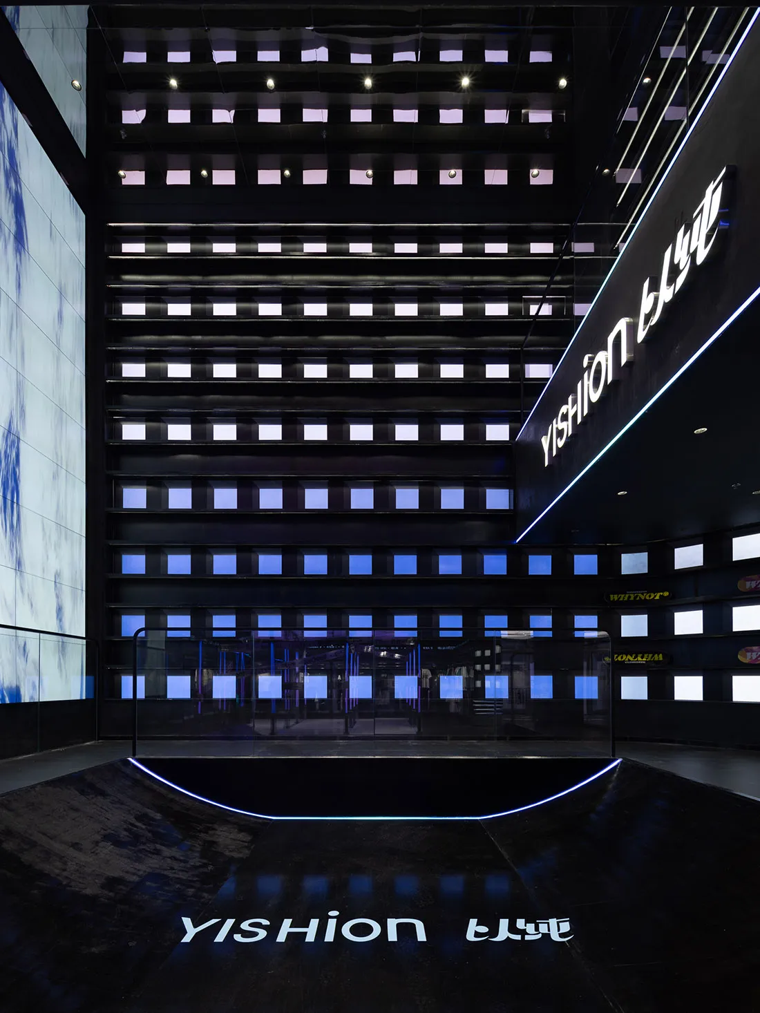 A modern shopping center interior featuring glass walls and bright neon lighting.