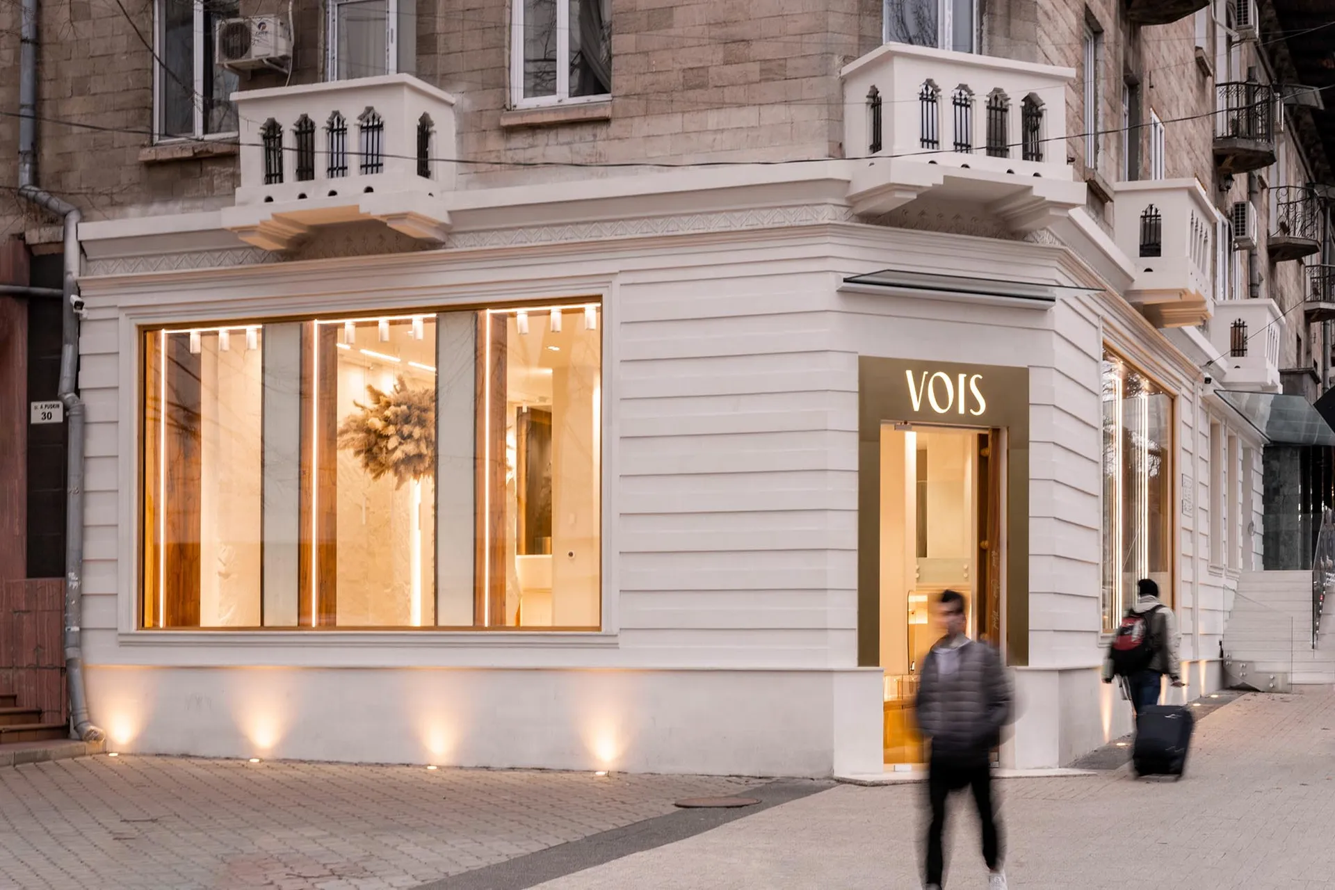 A modern retail storefront with a white stone exterior, illuminated by warm indoor lighting.