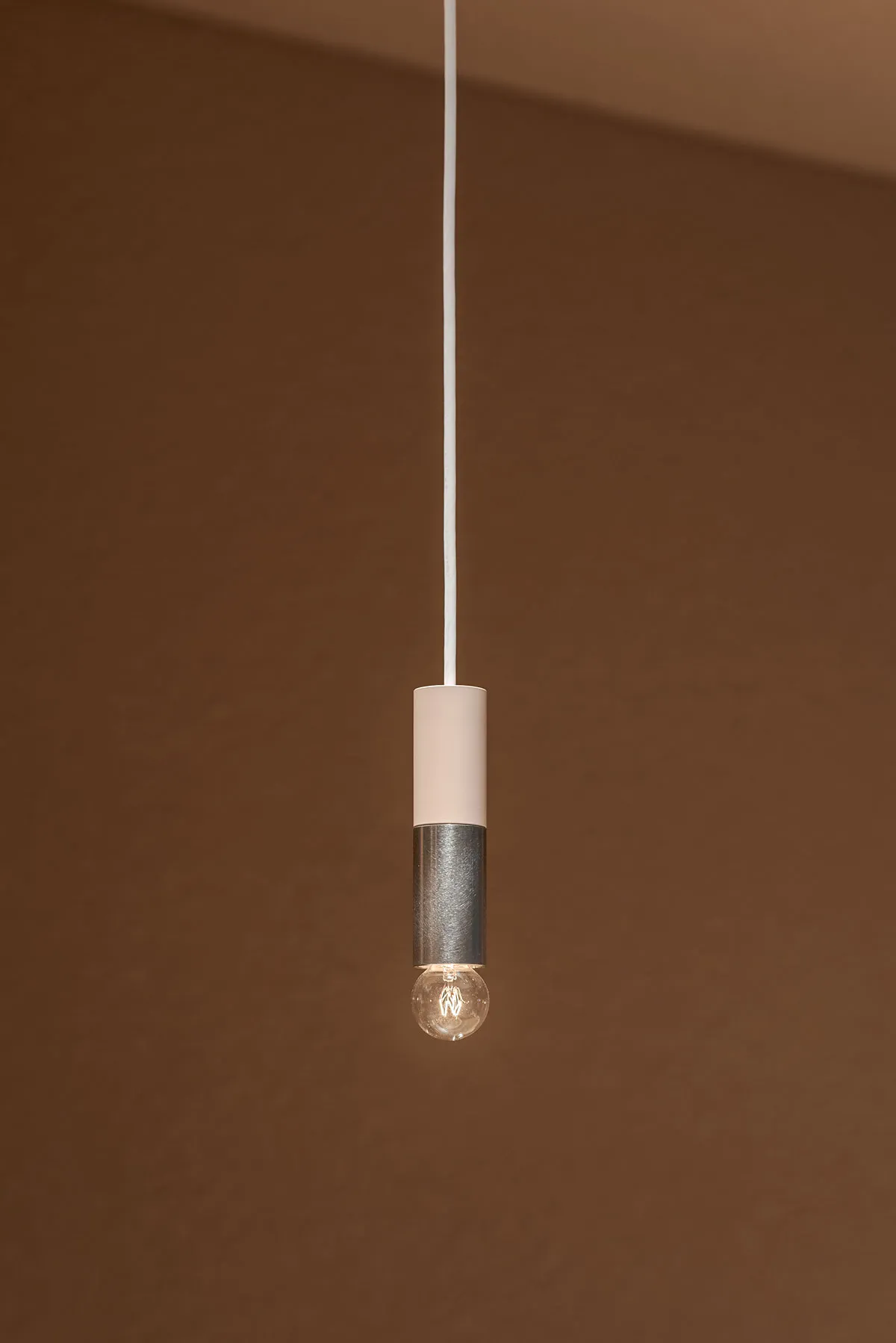 A minimalist light fixture featuring a metal cylinder with a single bulb.