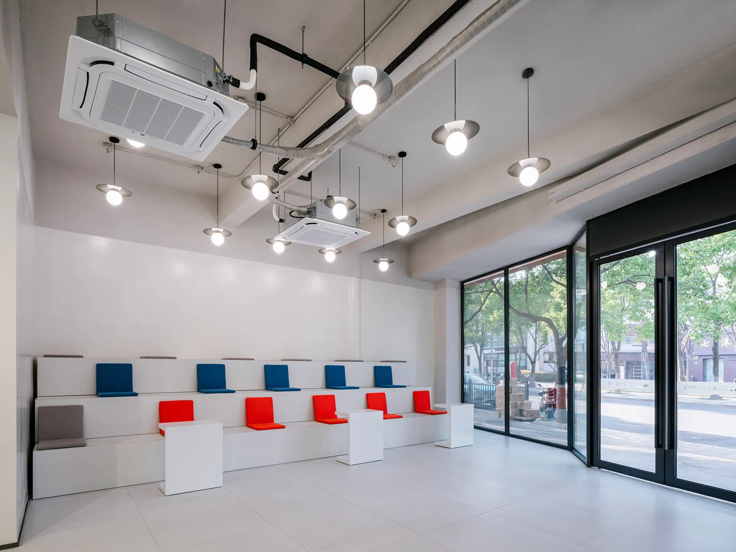 A minimalist waiting room with white concrete seating, orange and blue cushions, and pendant lights.