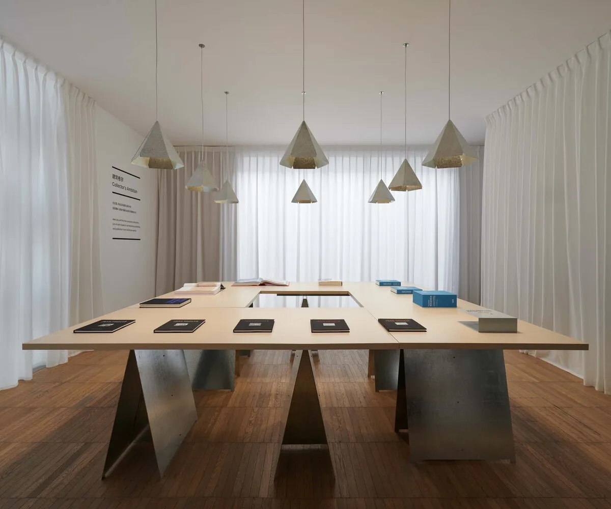 A minimalist conference room with a large wooden table, concrete bases, and six pendant lights hanging from the ceiling. The