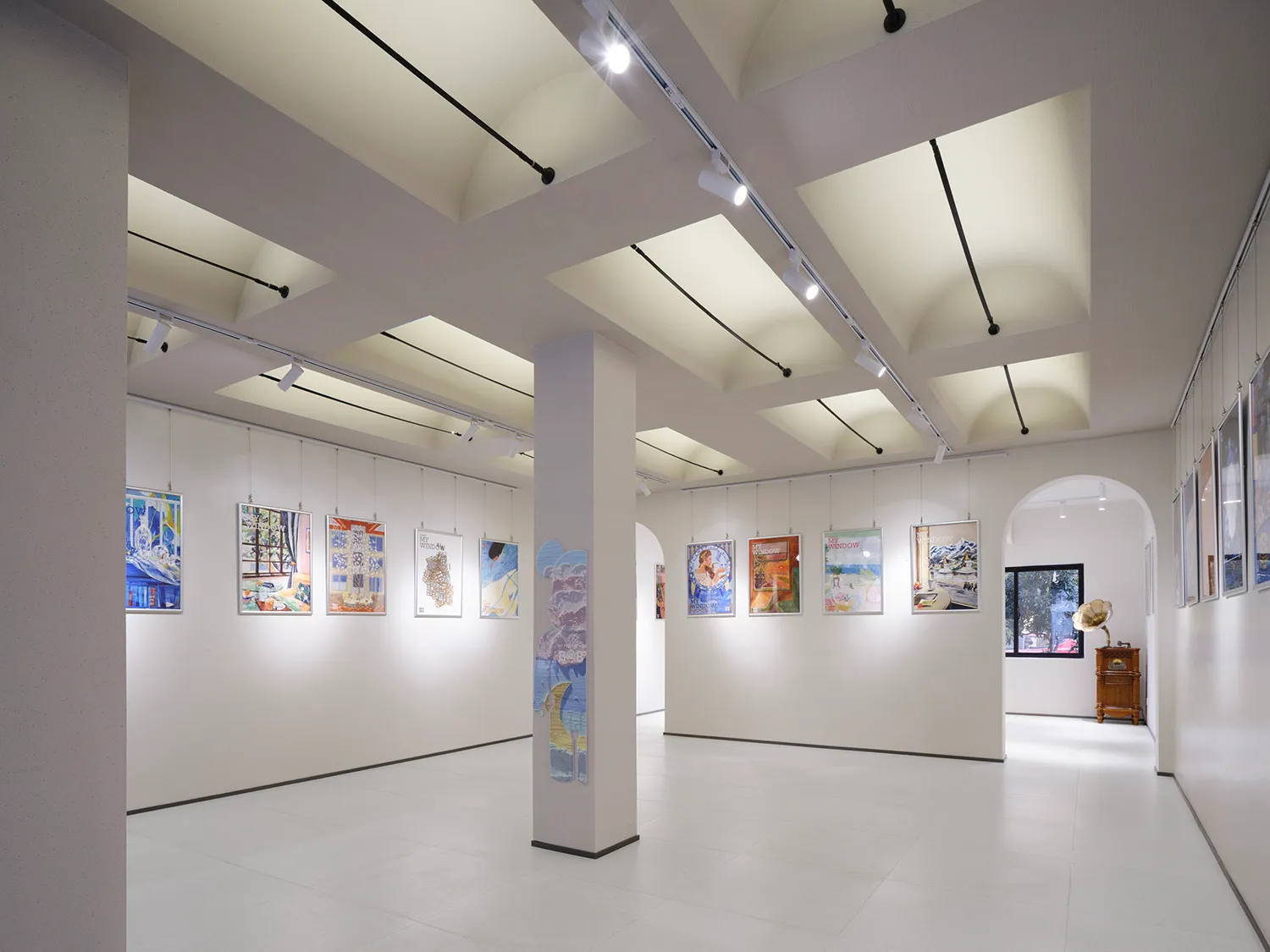 A modern art gallery with white walls, hanging paintings, and track lighting.
