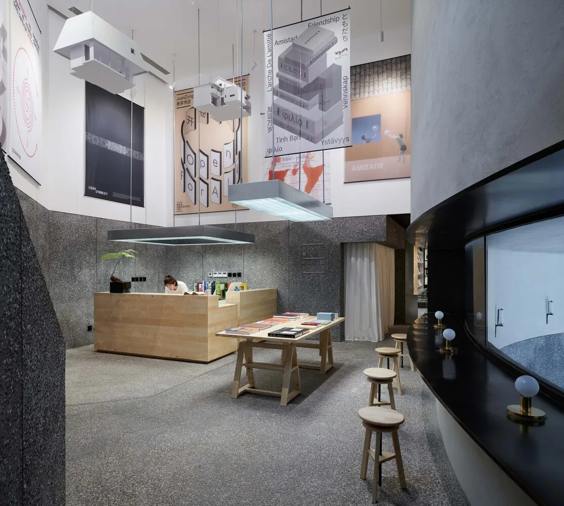 A modern library with books displayed on shelves, a counter with books and documents, and stools and tables.