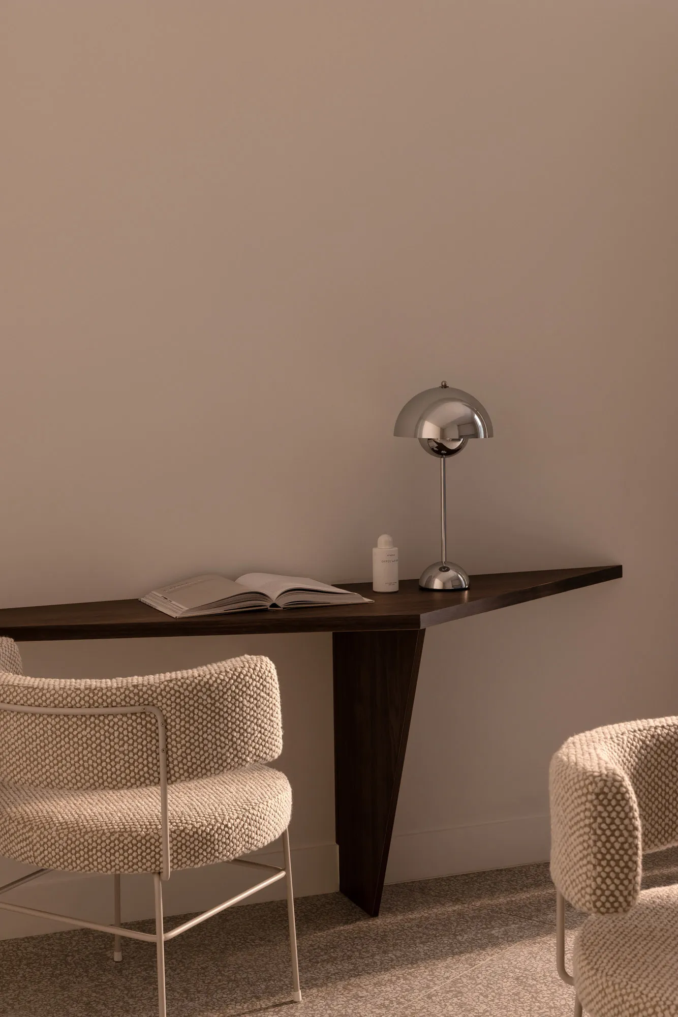 A minimalist office space featuring a modern wooden table with a book, lamp, and chair.