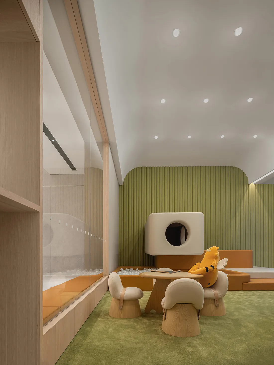 Modern minimalist children's playroom with wood furniture and green carpet, featuring a playful wooden structure with a圆形开口和柔